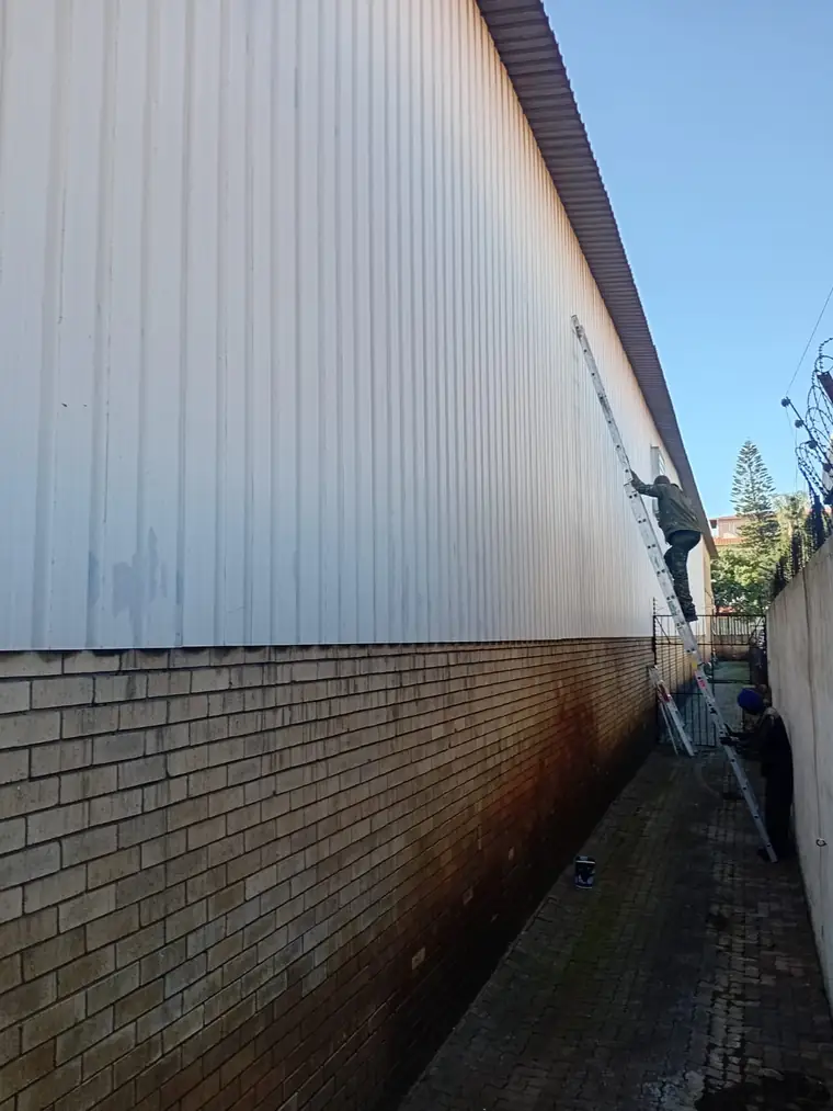 Painter on a ladder coating a large industrial wall above brickwork